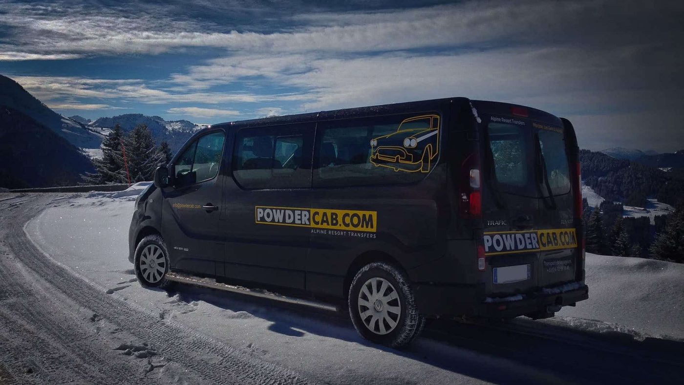 PowderCab minibus on a snowy mountain road beneath a dramatic winter sky